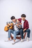 deux jeunes hommes étaient assis sur une chaise et jouaient de la guitare. photo