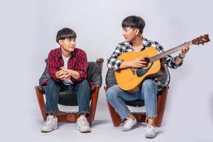 deux jeunes hommes étaient assis sur une chaise et jouaient de la guitare. photo