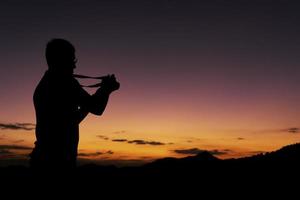 silhouette d'homme prenant une photo du lever du soleil depuis la montagne