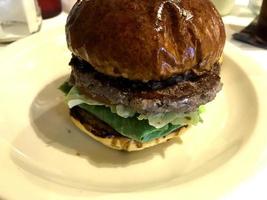 Burger de boeuf frais de rue avec pain brun, légumes, oeuf, bacon, fromage et sauces sur table. photo