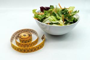 salade fraîche dans un bol et un ruban à mesurer. régime alimentaire et concept d'alimentation saine. photo