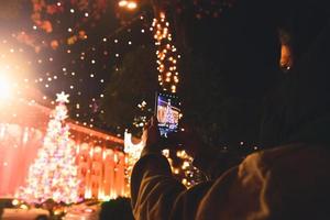 Jeune femme de race blanche tenir le téléphone et prendre une photo d'un arbre de Noël dans le centre-ville la nuit, Géorgie, Tbilissi