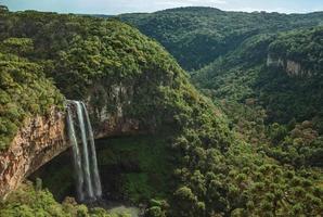 cascade de caracol tombant d'une falaise rocheuse formant une grotte face à un canyon couvert de forêt dans un parc près de canela. une charmante petite ville très appréciée par son écotourisme dans le sud du brésil. photo