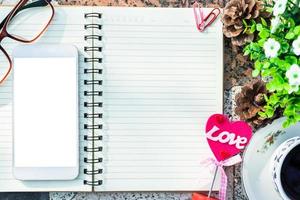 image vue de dessus d'un cahier vide, d'un smartphone, de lunettes et d'une tasse de café sur fond de sol en marbre. concept d'amour avec coeur de bureau, Saint-Valentin. photo