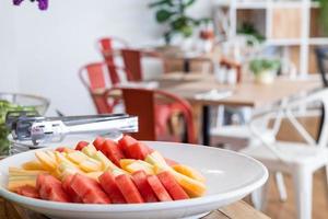 hacher les morceaux de pastèque et d'ananas dans un plat blanc la salle à manger et le vase à fleurs sur la décoration de la table au buffet en libre-service à l'hôtel. photo