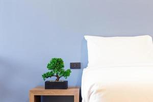 gros plan d'un oreiller blanc sur une décoration de lit avec lampe lumineuse et arbre vert dans des pots de fleurs à l'intérieur de la chambre de l'hôtel. photo