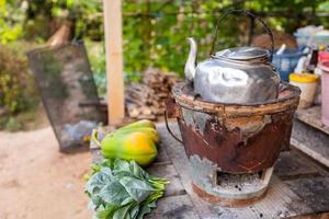 Une vieille bouilloire thaïlandaise sur un poêle à charbon thaïlandais avec des légumes à feuilles vertes et de la papaye posée sur une table en bois est un style de cuisine traditionnel thaïlandais. photo