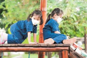 deux jeunes filles portant un masque blanc jouent à l'escalade sur un équipement en bois pour aire de jeux. pour prévenir les virus et les petites poussières toxiques que sont la pollution de l'air pm2.5. photo