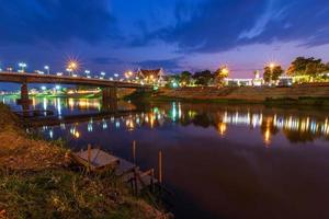 belle lumière sur la rivière nan la nuit sur le pont pont naresuan dans la ville de phitsanulok, thaïlande. photo