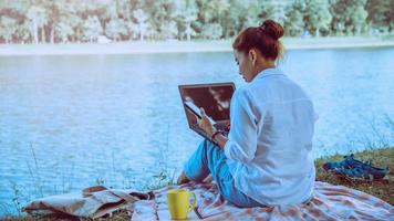 femmes assises au bord d'une rivière relaxante dans le parc. assis à travailler avec un cahier et à boire du café. Pendant les vacances photo