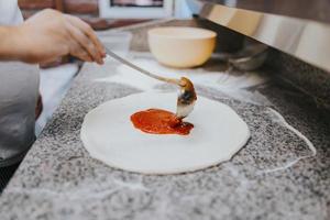 homme mettant la sauce tomate sur la pâte à pizza photo