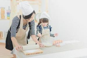 famille heureuse dans la cuisine. mère asiatique et sa fille préparant la pâte pour faire un cake.photo design pour la famille, les enfants et les gens heureux concept. photo