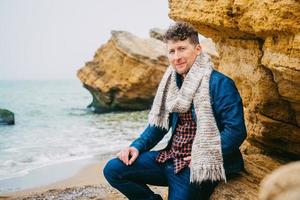 homme voyageur avec sac à dos debout sur une plage de sable au milieu des rochers sur fond de mer photo