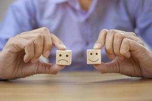 l'homme d'affaires en gros plan choisit le visage souriant et l'icône du visage triste sur le cube de bois. photo