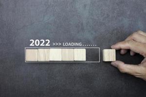 chargement du concept du nouvel an 2022, homme de main mettant le cube en bois sur la barre de processus. photo