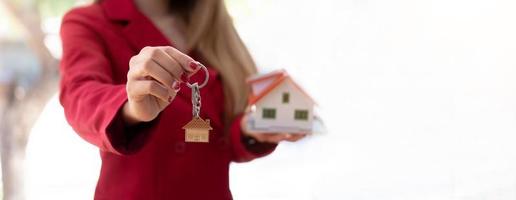 femme tenant un modèle de maison blanche et une clé de maison en main. approbation de prêt hypothécaire concept de prêt et d'assurance à domicile. photo