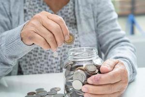 vieille dame asiatique âgée ou âgée tenant une pièce de monnaie comptant dans un bocal en verre. pauvreté, problème d'épargne à la retraite. photo