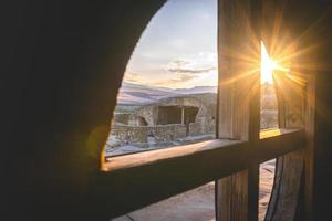 vue depuis le cadre de fenêtre en bois jusqu'à la structure de la ville troglodyte d'uplistsikhe à l'extérieur pendant le coucher du soleil