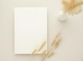 maquette de carte d'invitation blanche avec une herbe séchée et un vase en céramique sur fond beige, composition minimale du lieu de travail beige, mise à plat, maquette photo