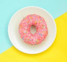 Donut glaçures rose sur plaque blanche sur fond turquoise jaune pastel photo