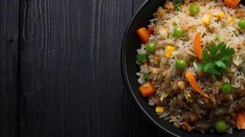 frit riz avec poulet et des légumes dans une noir bol sur une noir en bois Contexte. photo