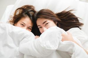 belles jeunes femmes asiatiques lgbt couple heureux lesbien étreignant et souriant en position couchée ensemble dans son lit sous une couverture à la maison. femmes drôles après le réveil. couple de lesbiennes lgbt ensemble concept à l'intérieur. photo