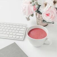 espace de travail blanc avec carnet de notes rose clair et fleur blanche avec café sur table blanche. photo