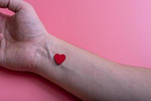 coeur au poignet d'une main d'homme sur fond rose. photo