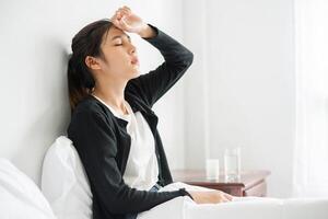 une femme mal à l'aise est assise sur le lit et a des médicaments sur la table. photo