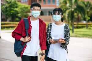 les étudiants masculins et féminins portent des masques et se tiennent devant l'université. photo