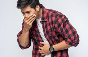un homme debout avec un mal d'estomac met ses mains sur son ventre et se couvre la bouche.
