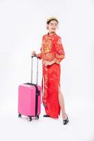 une femme porte un costume cheongsam avec une couronne prête à voyager avec un sac de voyage rose au nouvel an chinois