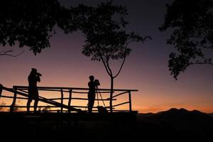 silhouette de photographe sur la montagne prenant des photos de paysage avec coucher ou lever de soleil - femme photographe avec appareil photo