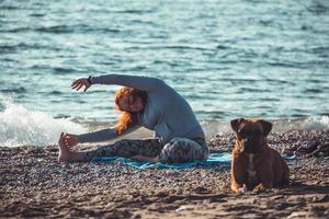 fille faisant du yoga et s'étirant sur la plage avec son chien photo