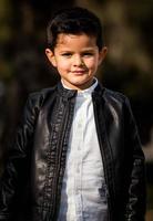 mode petit garçon vêtu d'une veste en cuir. parc ou forêt, extérieur photo