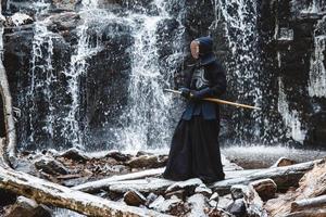 homme pratiquant le kendo avec une épée de bambou sur fond de cascade, de rochers et de forêt photo