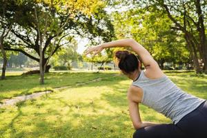 Une jeune femme asiatique en bonne santé réchauffe le corps en s'étirant avant l'exercice et le yoga près du lac au parc sous une lumière chaude et légère le matin. mode de vie fitness et femmes actives s'exercent dans le concept de ville urbaine.