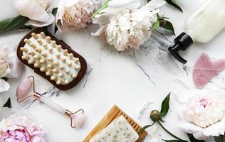 produits de beauté. rouleau facial, huiles essentielles, brosse de massage et belles pivoines sur fond de marbre blanc. photo