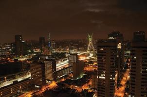 vue nocturne sur les toits de la ville avec pont et bâtiments sous nuageux et pleine lune dans la ville de sao paulo. la ville gigantesque, célèbre pour sa vocation culturelle et commerciale. photo