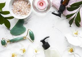 Massage du visage rouleau de jade avec produit cosmétique sur fond de marbre blanc photo