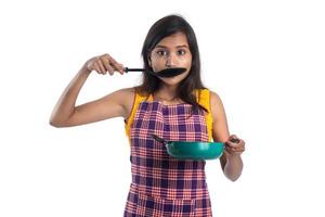 jeune femme indienne tenant une cuillère d'ustensiles de cuisine, une stapule, une louche et une casserole, etc. sur fond blanc photo