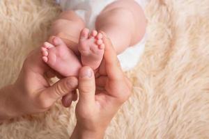 papa tient dans ses mains un petit baby foot. petites jambes d'un nouveau-né dans les grandes mains de papa. massage des pieds de bébé photo