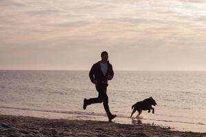 jeune homme marchant sur la plage du matin avec chien noir photo