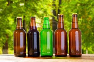 bière sur table sur fond de forêt floue, boissons d'été, bouteilles colorées photo
