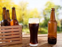 tasse de bière brune et de bouteilles sur une boîte en bois sur une table sur fond de parc flou photo