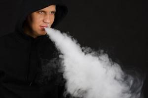 vapotant un homme blanc tenant un mod. un nuage de vapeur. fond noir. vapoter une cigarette électronique avec beaucoup de fumée. concept de vape mise au point sélective de l'espace de copie photo