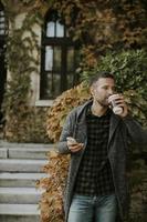 jeune homme utilisant un téléphone portable et tenant un café à emporter dans le parc photo