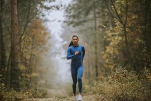 Jeune femme courant vers la caméra sur le sentier forestier à l'automne photo