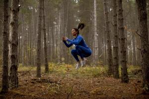 Jeune femme prenant le saut en hauteur sur le sentier forestier à l'automne photo