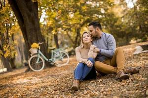 Jeune couple assis sur le sol dans le parc d'automne photo